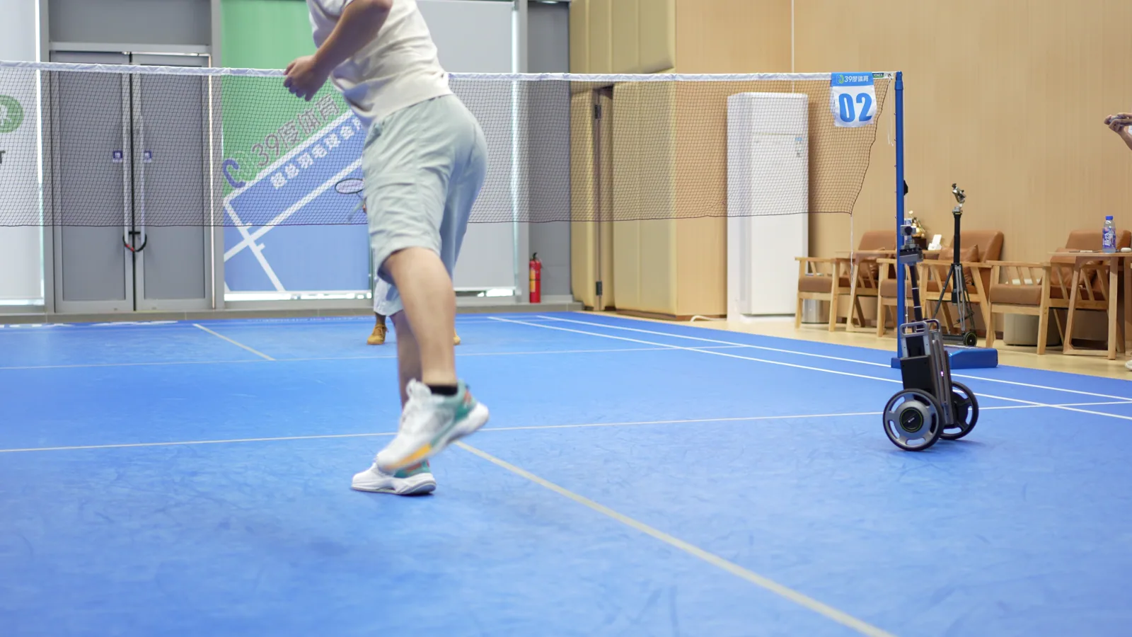 CineyBot in use beside badminton players on an indoor court