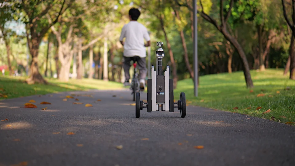 CineyBot following a cyclist along a sunlit park path